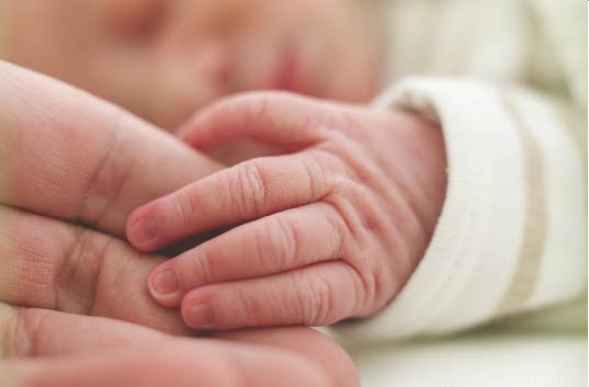 Mother holding sleeping baby hand.